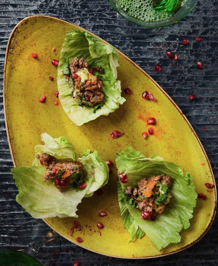 Lettuce Cups with Lamb Three lettuce cups with lamb on a yellow plate, staged on a black background.