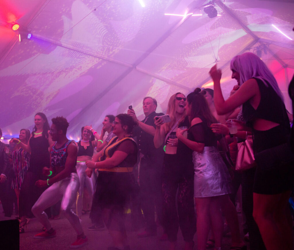 A group of people dance on the pink lit dance floor of Pittsburgh's Mattress Factory pink party.