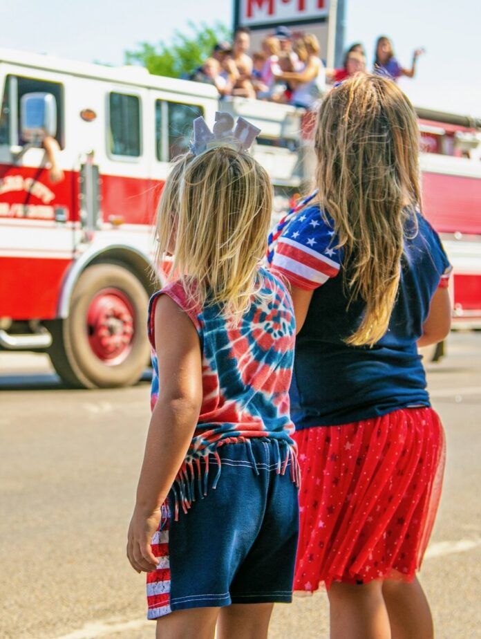 Two girls in red white and blue clothes watch a firetruck drive by during a Memorial Day Parade event in Pittsburgh.