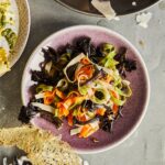 In a pink bowl is multicolor fettuccine with black trumpet mushroom sauce, sitting on a grey table.