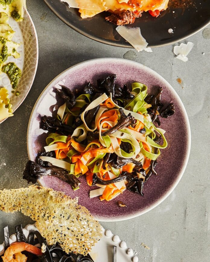 In a pink bowl is multicolor fettuccine with black trumpet mushroom sauce, sitting on a grey table.
