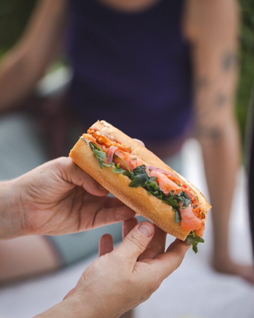 A person holds a sandwich with meats and greens.