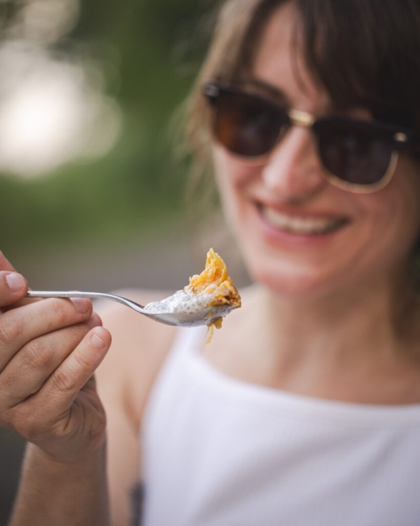 A woman with brown sunglasses smiles at a spoon in front of her face.