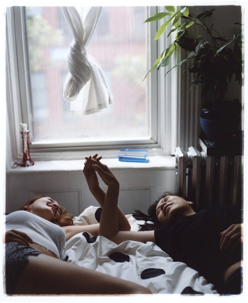 Two girls hand intertwined looking up at a ceiling in a bedroom.