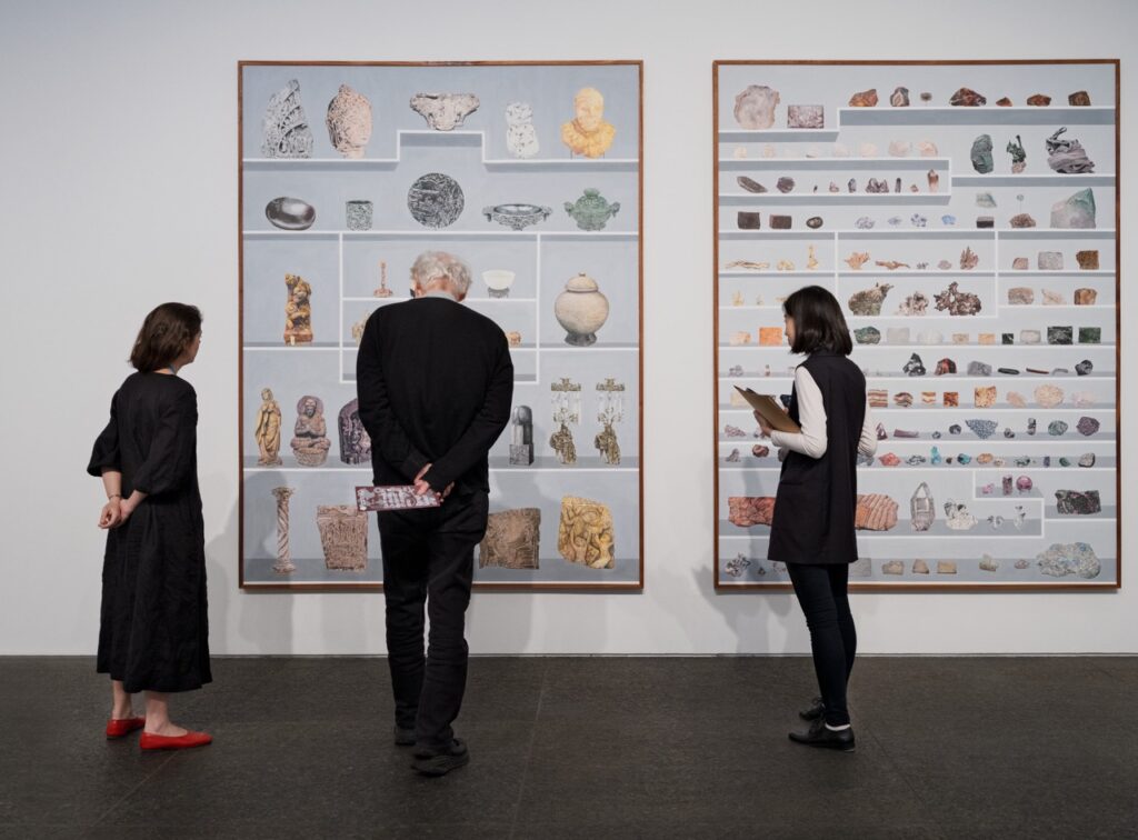 Three people in black look at Pittsburgh art show painting featuring shelves or objects.