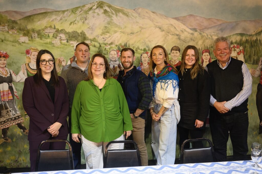A group of seven people stand in front of a painting of a mountain range.