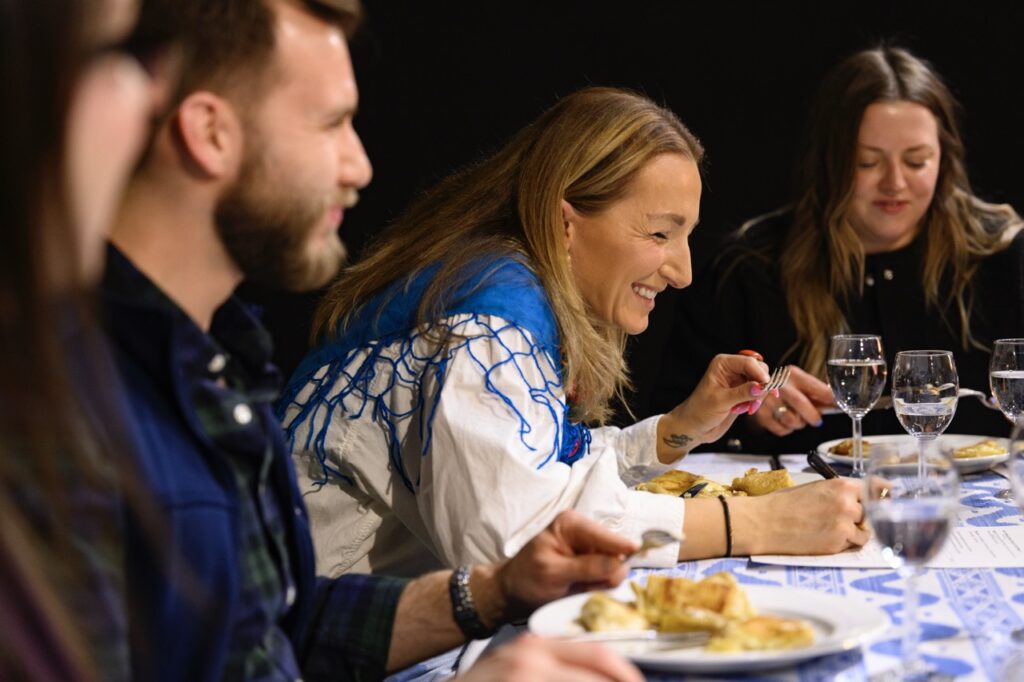 A woman in white and blue laughs at a table full of Pittsburgh's pierogis.