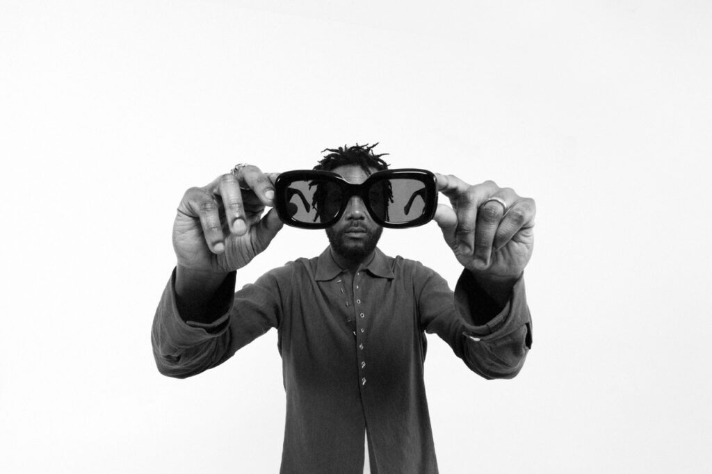 A man holding up sunglasses to the camera.