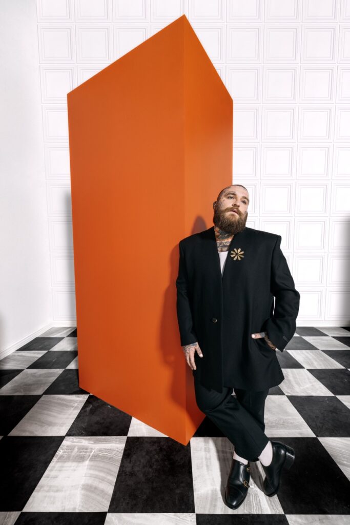 A man in a suit stands in front of an orange block on a checkerboard floor.