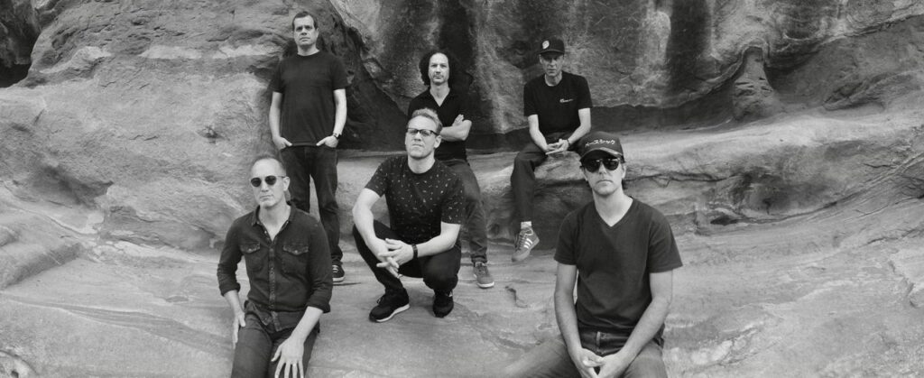6 men in black clothes stand in front of a cliff.