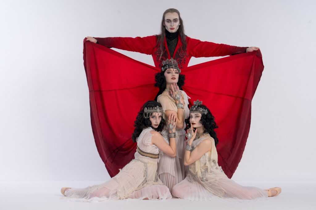 A group of dancers for Pittsburgh's Dracula sit together on the floor with Dracula in red behind them.