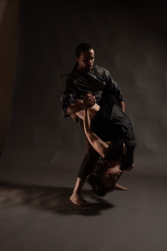 A man and woman in black dance together on a dark black background.
