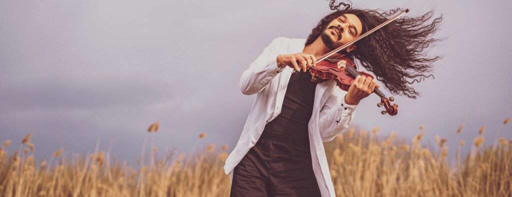 A man playing violin in a wheat field in a white jacket.