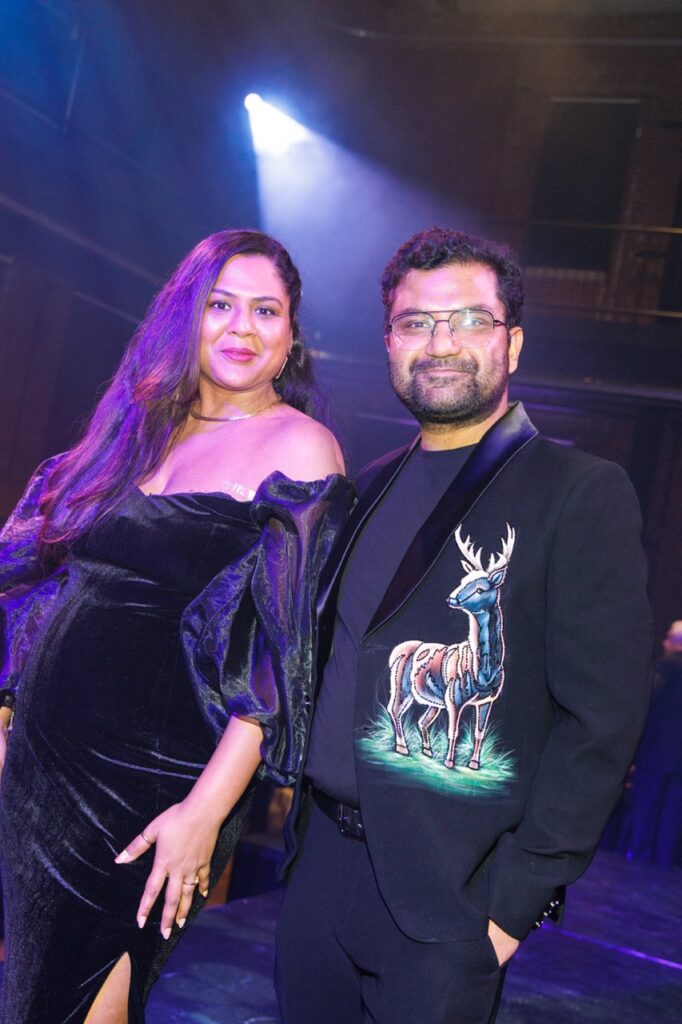 A man in a deer jacket and woman in a black gown stand together under a spotlight.