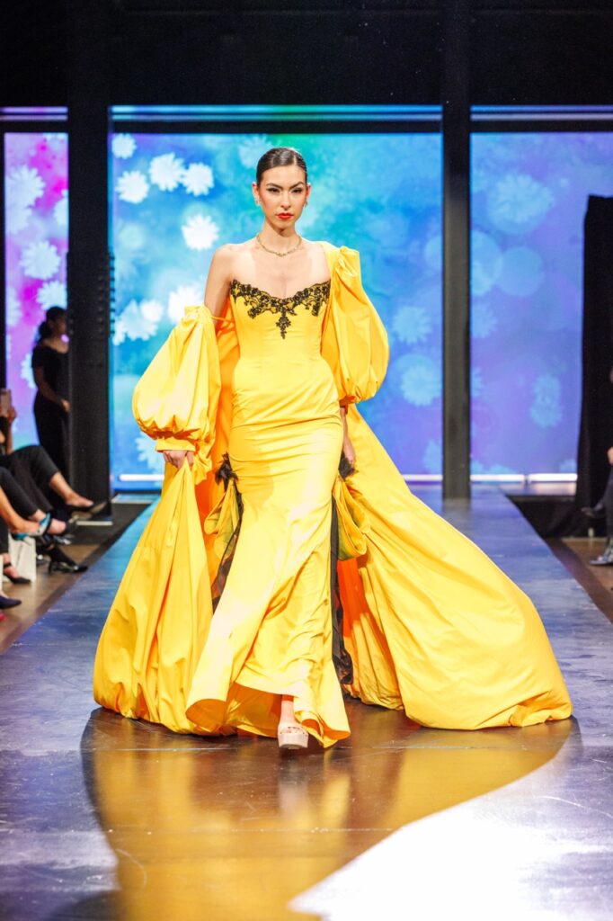 A woman in a yellow gown walks down a runway.