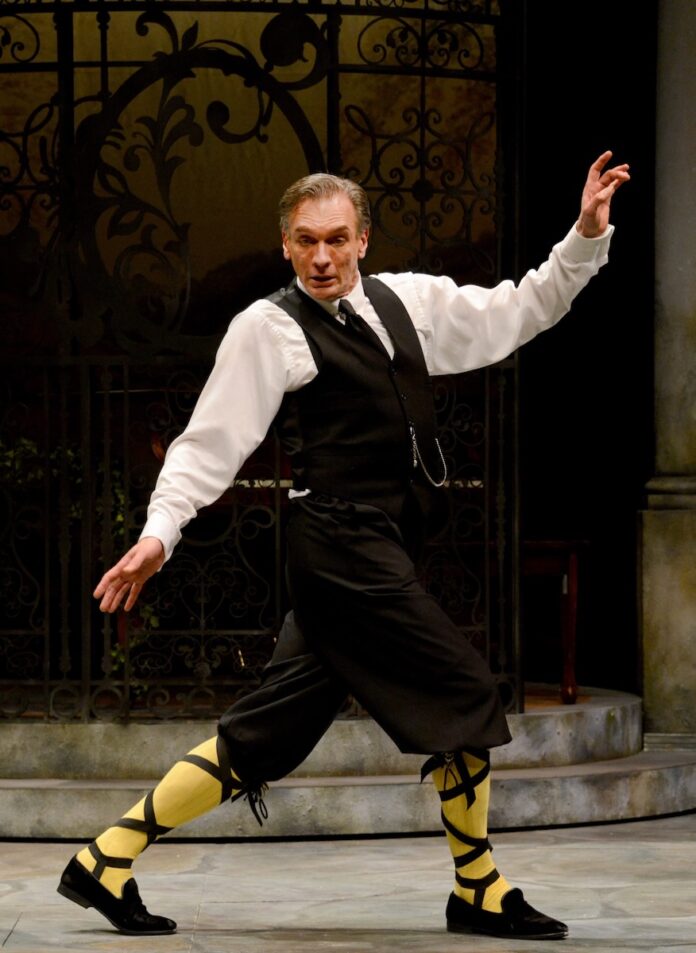 A man in a white button up shirt, black vest, and black pants dances on stage at a Pittsburgh summer theater performance.