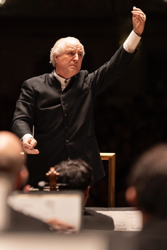 A conductor raises his hand up with a fist, wand in his other hand.