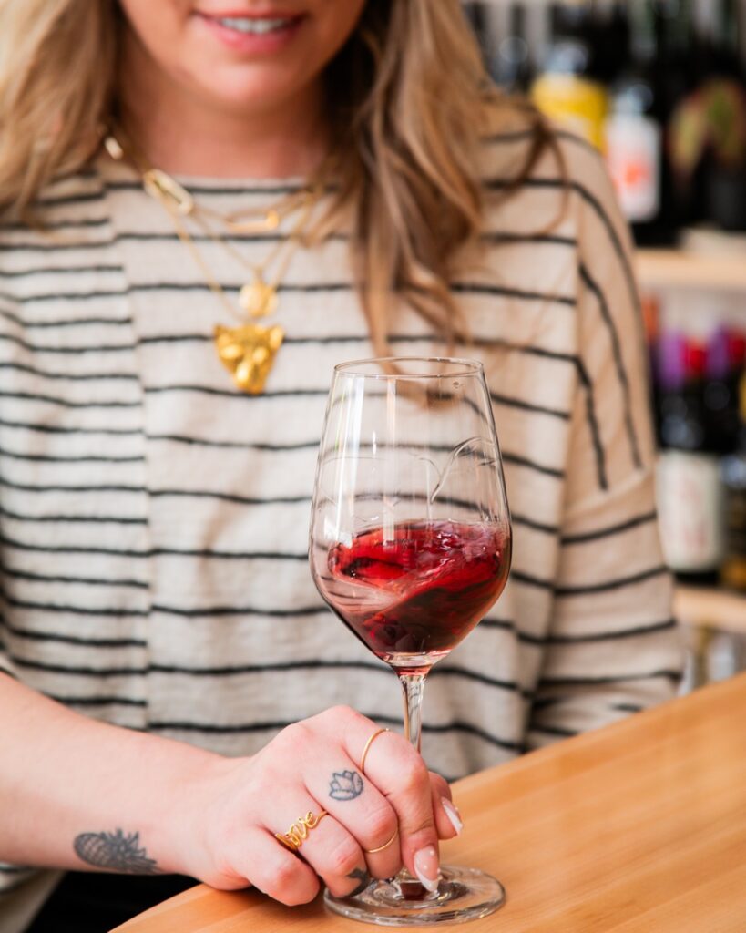 A woman swirls a wine glass on a wood table.