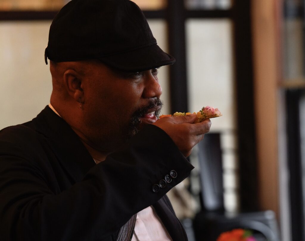 A man in a black hat holds a forkful of food up to his mouth.