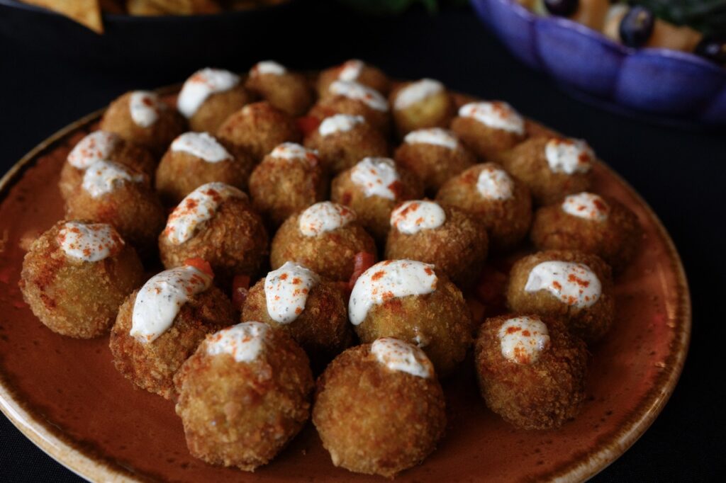 Small fried brown bals with a white sauce on top sit on a red plate.
