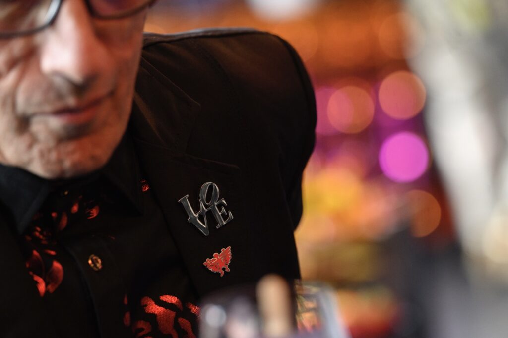 A man leans forward with a LOVE pin in silver on his jacket.