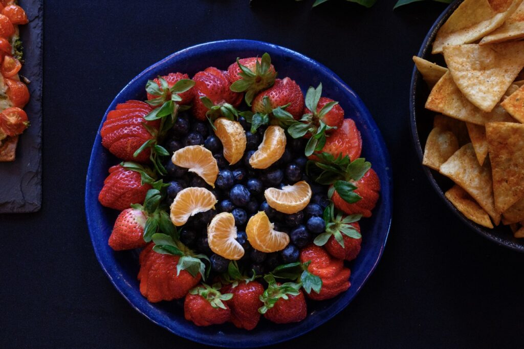 A blue platter with rounds of fruit like strawberries, blueberries, and mandarin orange pieces.
