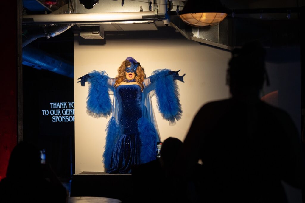 A woman performs on a stage in a blue gown and masquerade mask.