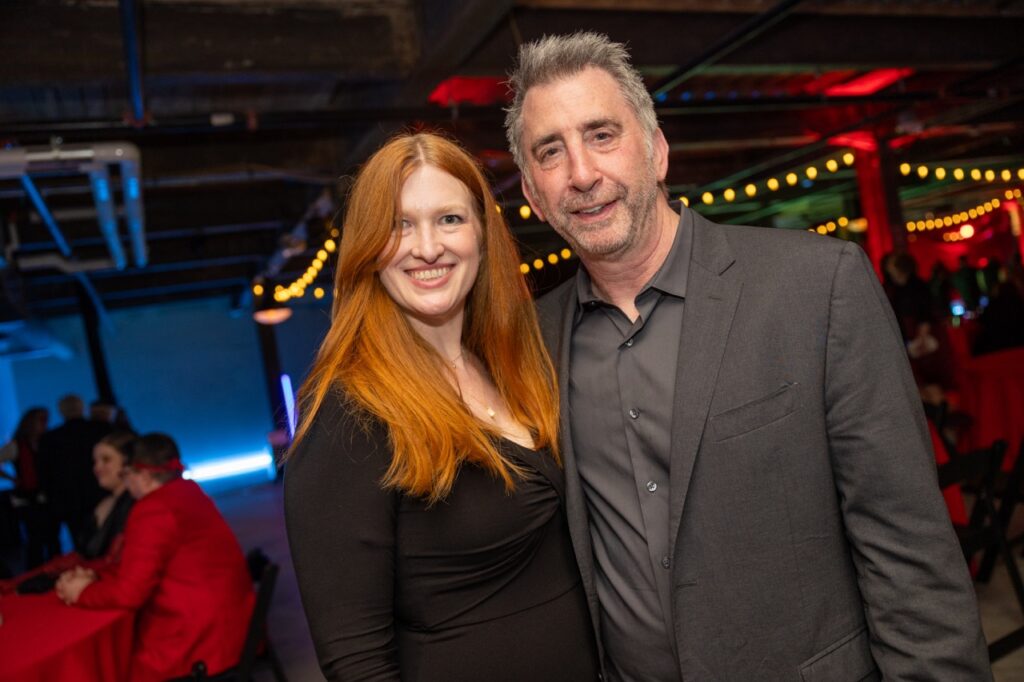 A woman with ginger hair stands with a man with grey hair and a grey suit jacket.