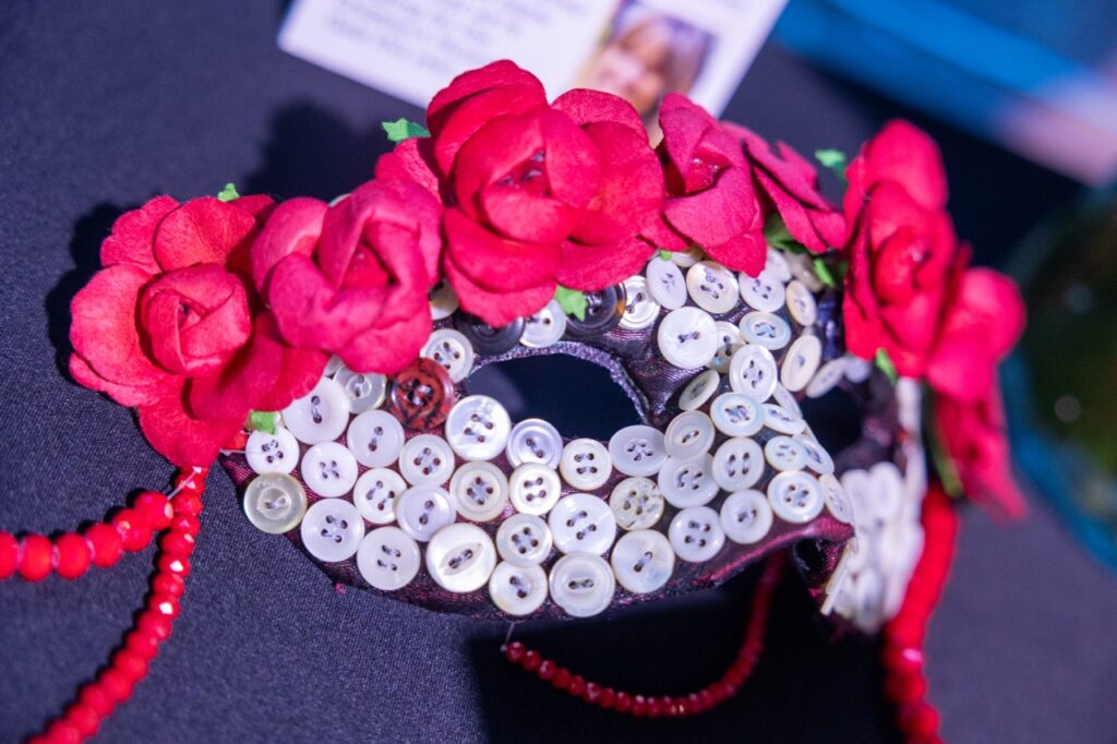 A masquerade mask covered in small white buttons and red flowers.