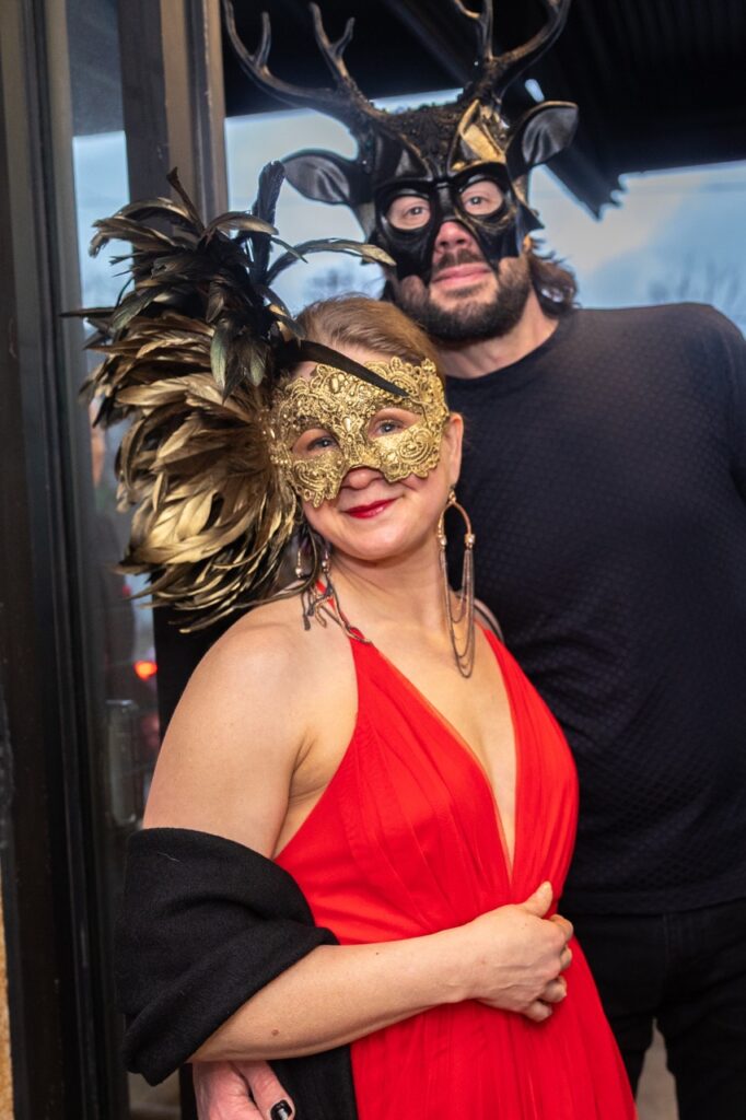 A man in a black masquerade mask and a woman in a lavish gold and black feather mask.