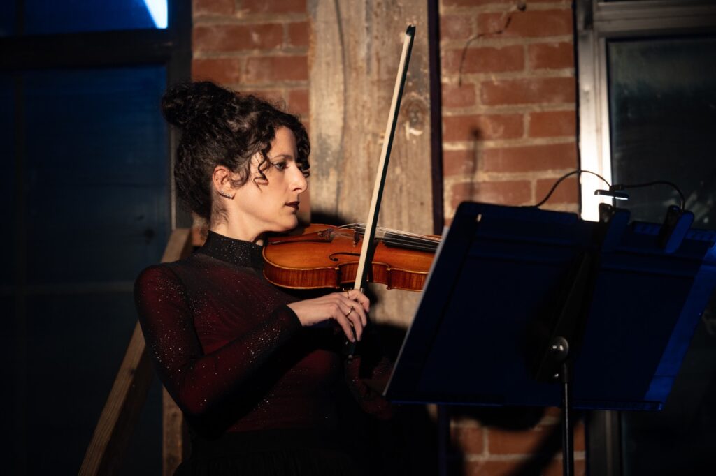 A woman with a violin plays in the corner of Quantum's Q Ball.