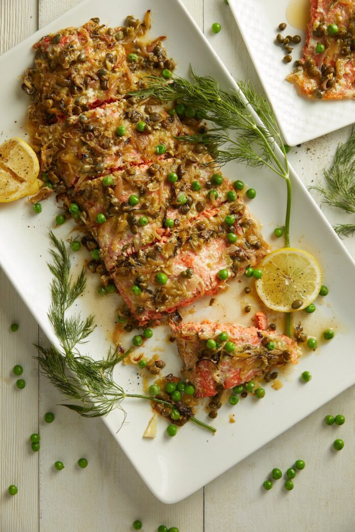Salmon with Dill Butter Sauce and English Peas Salmon with Dill Butter Sauce and English Peas served on a white tray with herbs and lemons