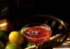 Sangre Sunset Sangre Sunset cocktail sits red in a coupe glass with a toothpick of blueberries floating on top.