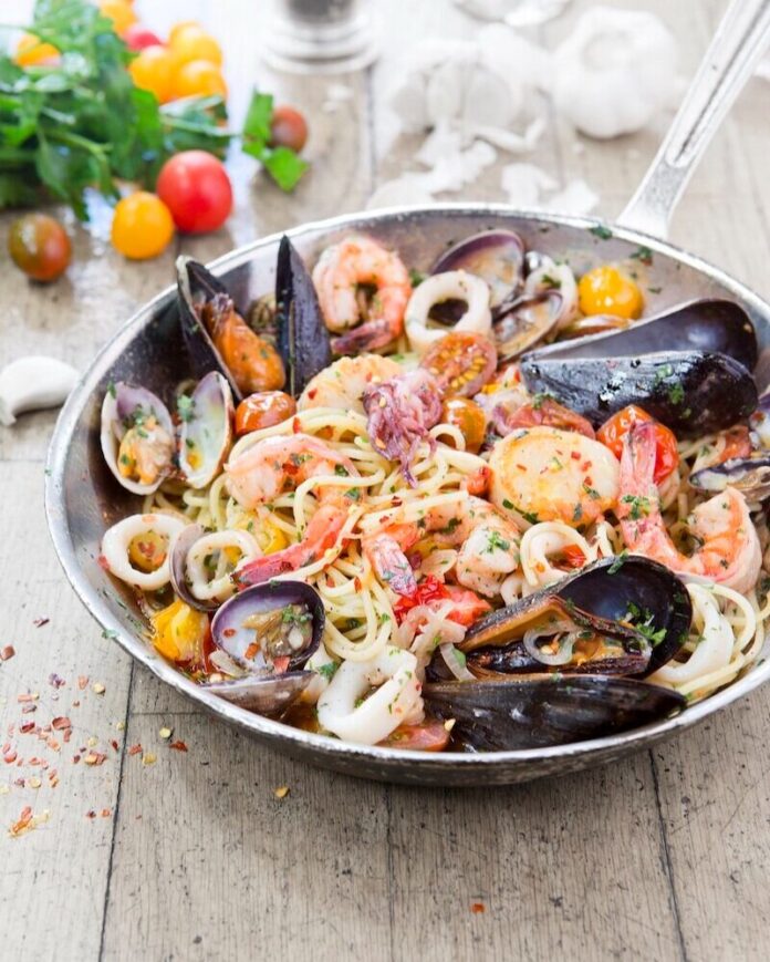 Seafood Spaghetti A seafood spaghetti sits in a shallow bowl with shrimp and mussels, all sitting on a wood picnic table.
