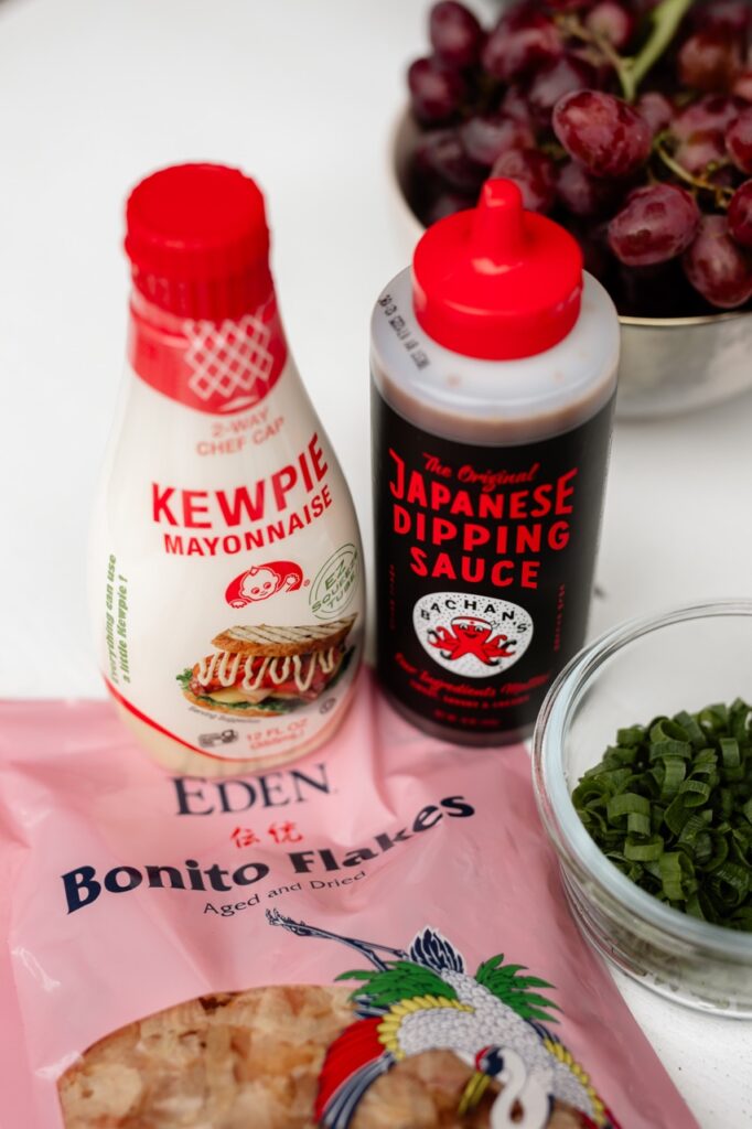 A bottle of Kewpie mayo and Japanese Dipping Sauce sit next to each other on top of Bonito Flakes.