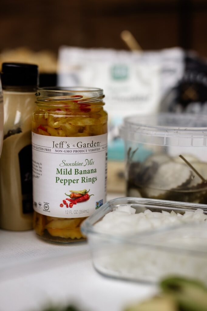 A jaw of pepper rings sits next to a container of onions.