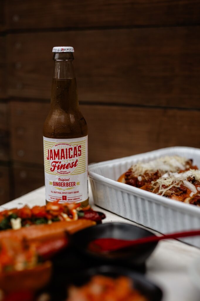A bottle of ginger beer sits amongst a tray full of gourmet hot dogs.
