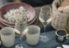 Spaghetti with Clams A red bowl with Spaghetti with Clams sits on a greenish tablecloth with a wine glass, candles, and another bowl of pasta behind it.