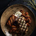 A swordfish with pork belly dish on a black plate.