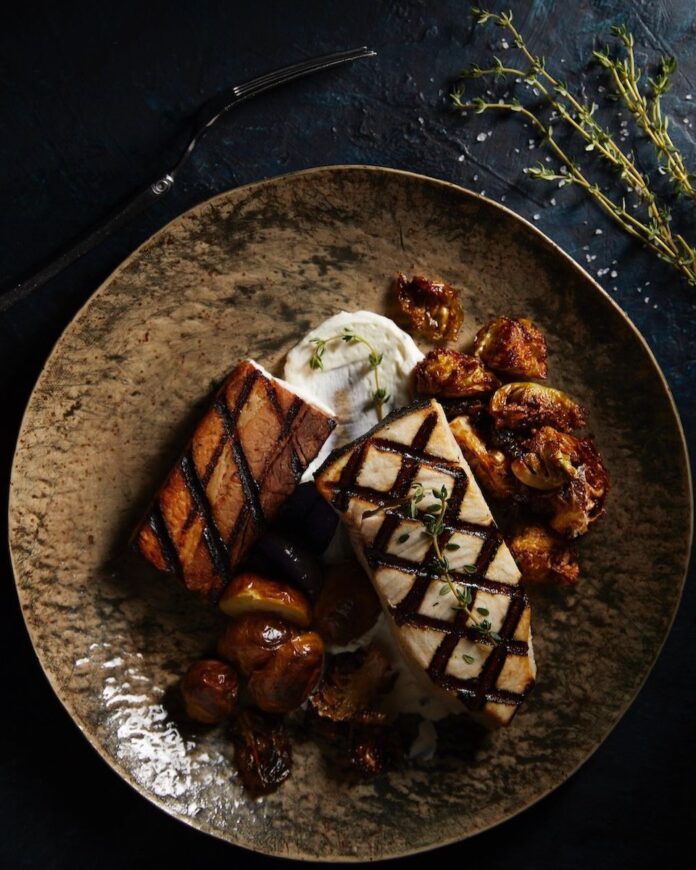 Swordfish with Pork Belly A swordfish with pork belly dish on a black plate.