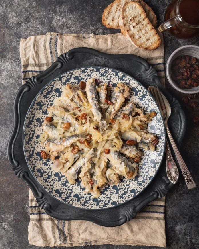 Sarde in Saor Sarde in Saor on a porcelain plate set on a rustic table.
