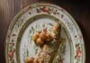 Whole Roasted Branzini A whole roasted branzini with fingering roasted potatoes sits on a white decorated plate with bits of orange and green flowers.