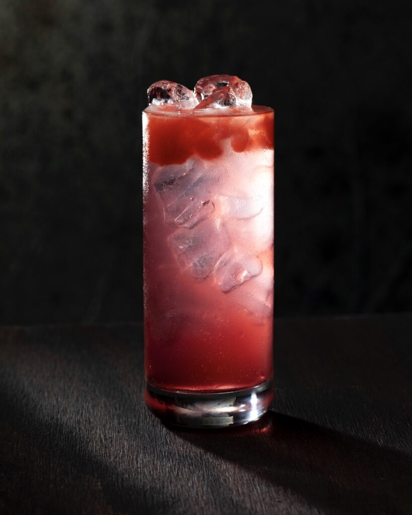 A clear cocktail with red juice spilling down the sides of the glass.