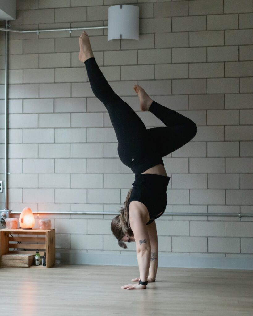 A woman in black yoga pants and sports bra does a hand stand with her feel in the air at a class in Pittsburgh.