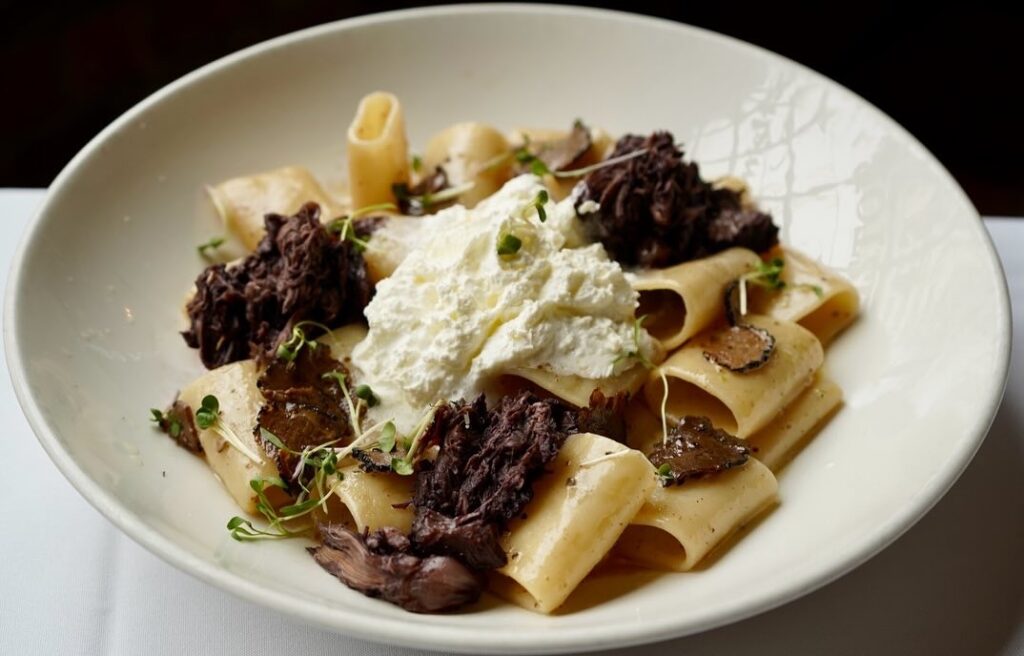 A white plate holds a pasta and beef dish from a Pittsburgh restaurant with ricotta cheese on top.