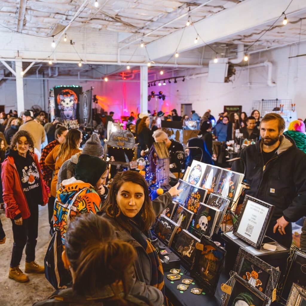 A large group of people look over tables of vendors and crafts at a night market event in Pittsburgh.