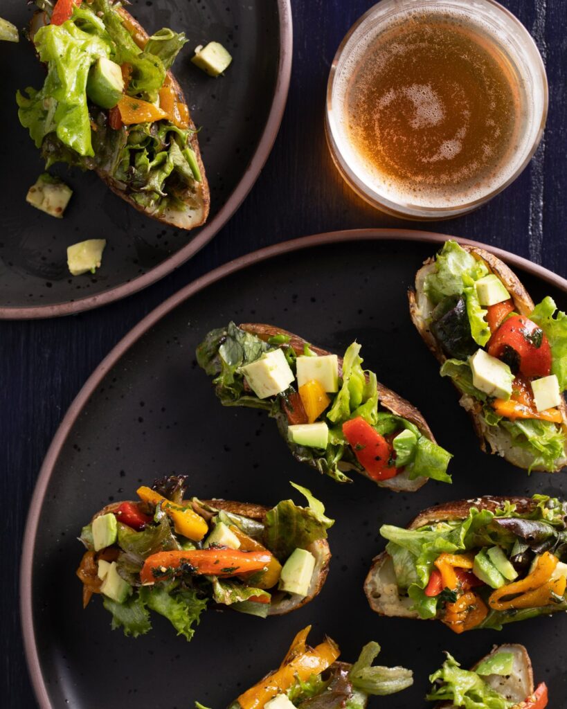 Small potato boats filled with salad on a black surface with a glass of beer on the side.