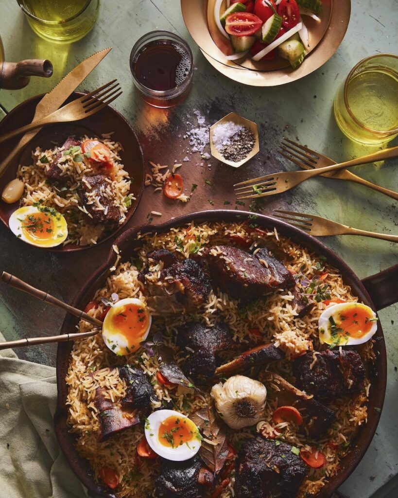 A beef short rib plov for navrus sits in a big dish with rice, beef short rib, and boiled eggs cut in half.