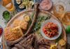 TABLE Magazine’s Ultimate Guide to Summer A brown platter holds various summer grilling items such as cornbread, steak, asparagus, corn, peppers, and much more fresh ingredients spread around the platter.