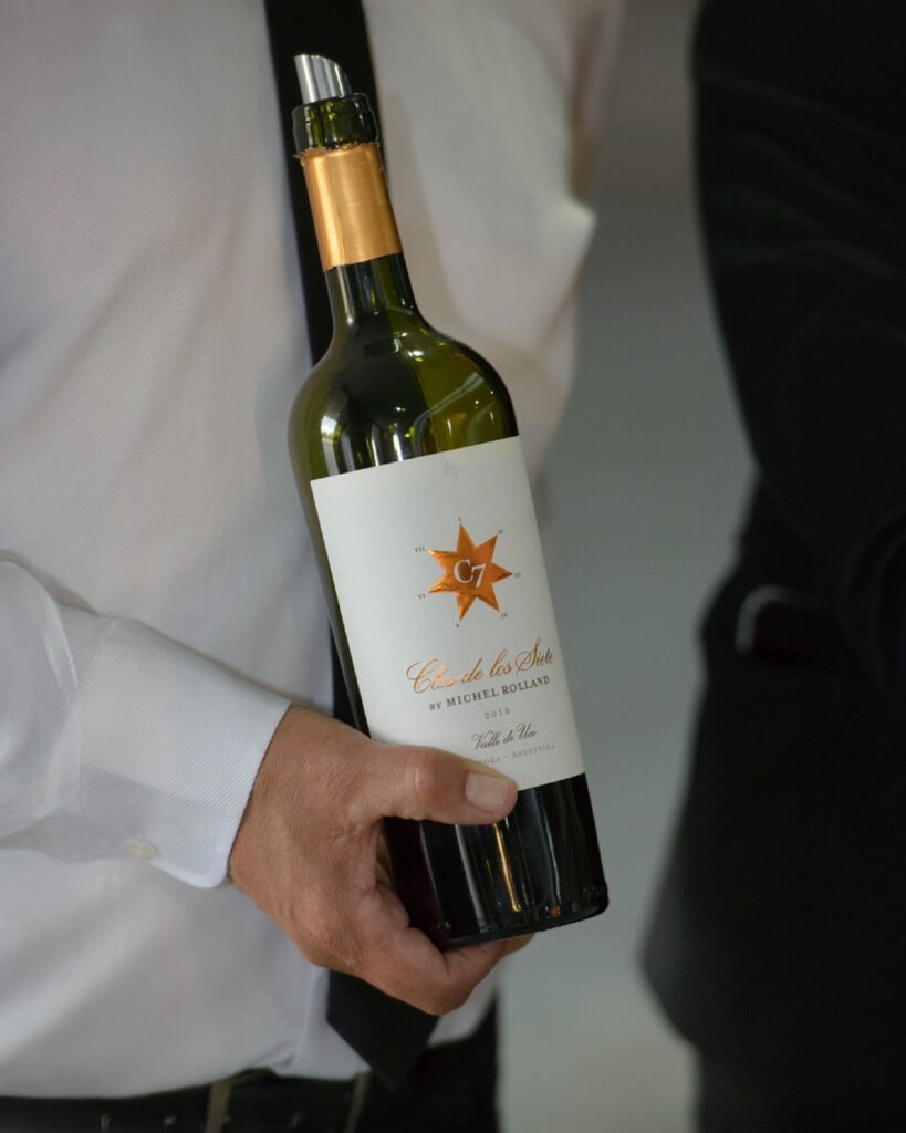 A man in a white dress shirt and tie holds a bottle of wine with a white label.